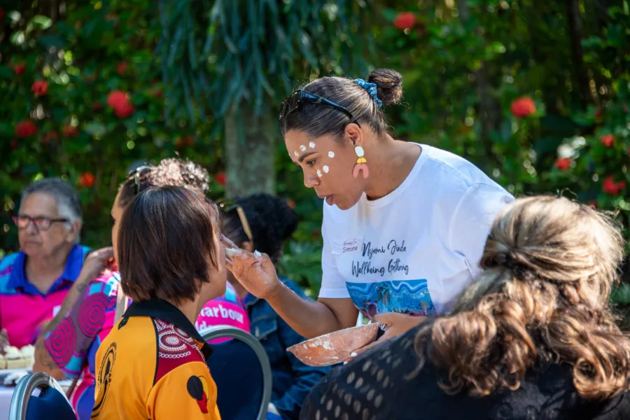 Community member carefully painting another person’s face at a welcoming outdoor gathering
